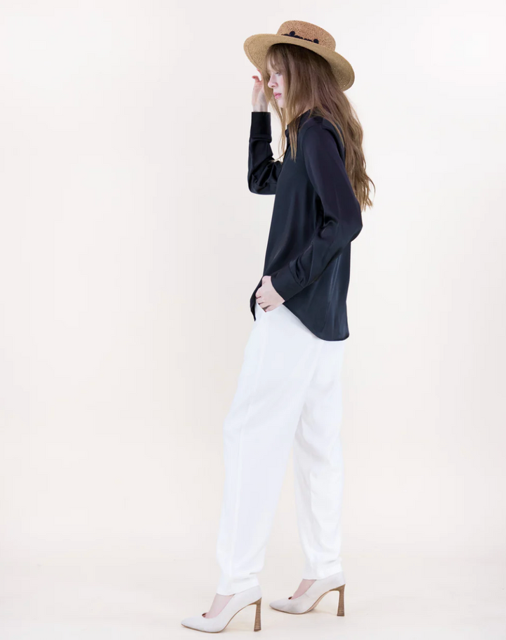 Woman wearing a black top, white pants, and a straw hat against a plain background