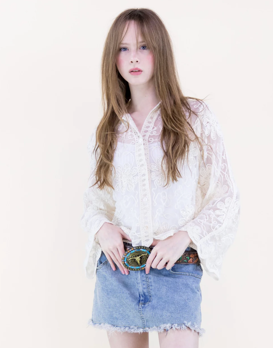 Woman wearing a beige lace blouse and denim skirt on a white background