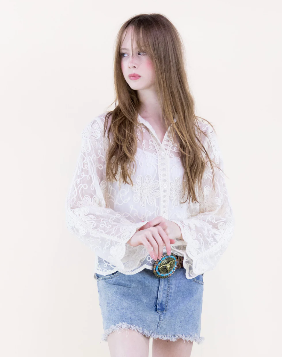Woman wearing a beige lace blouse and denim skirt on a white background