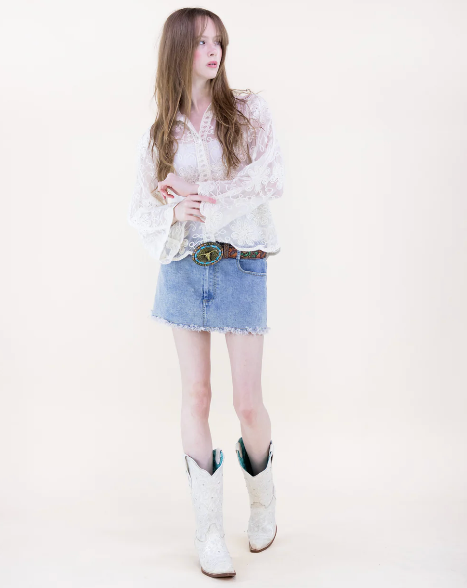 Woman wearing a beige blouse, denim skirt, and white cowboy boots on a white background