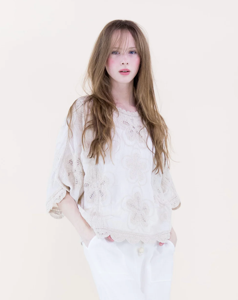 Woman wearing a white lace top and pants against a plain background
