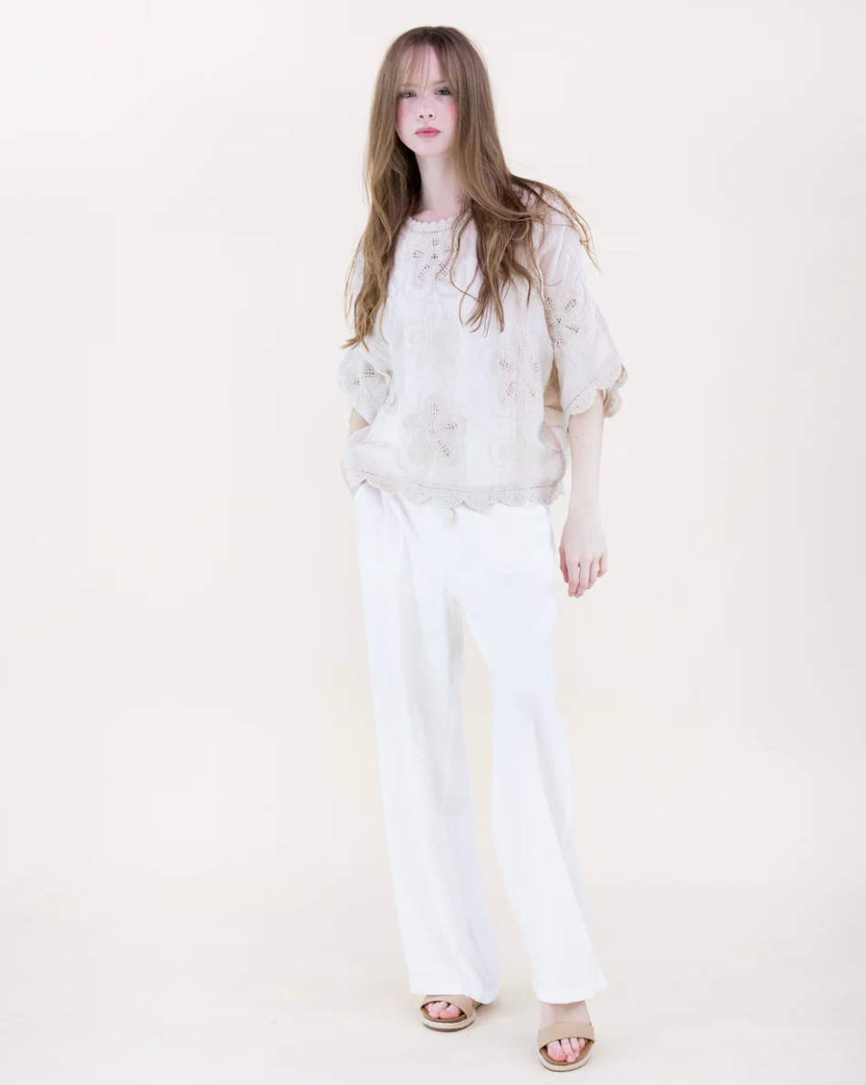 Woman wearing a light-colored top and white pants on a plain background