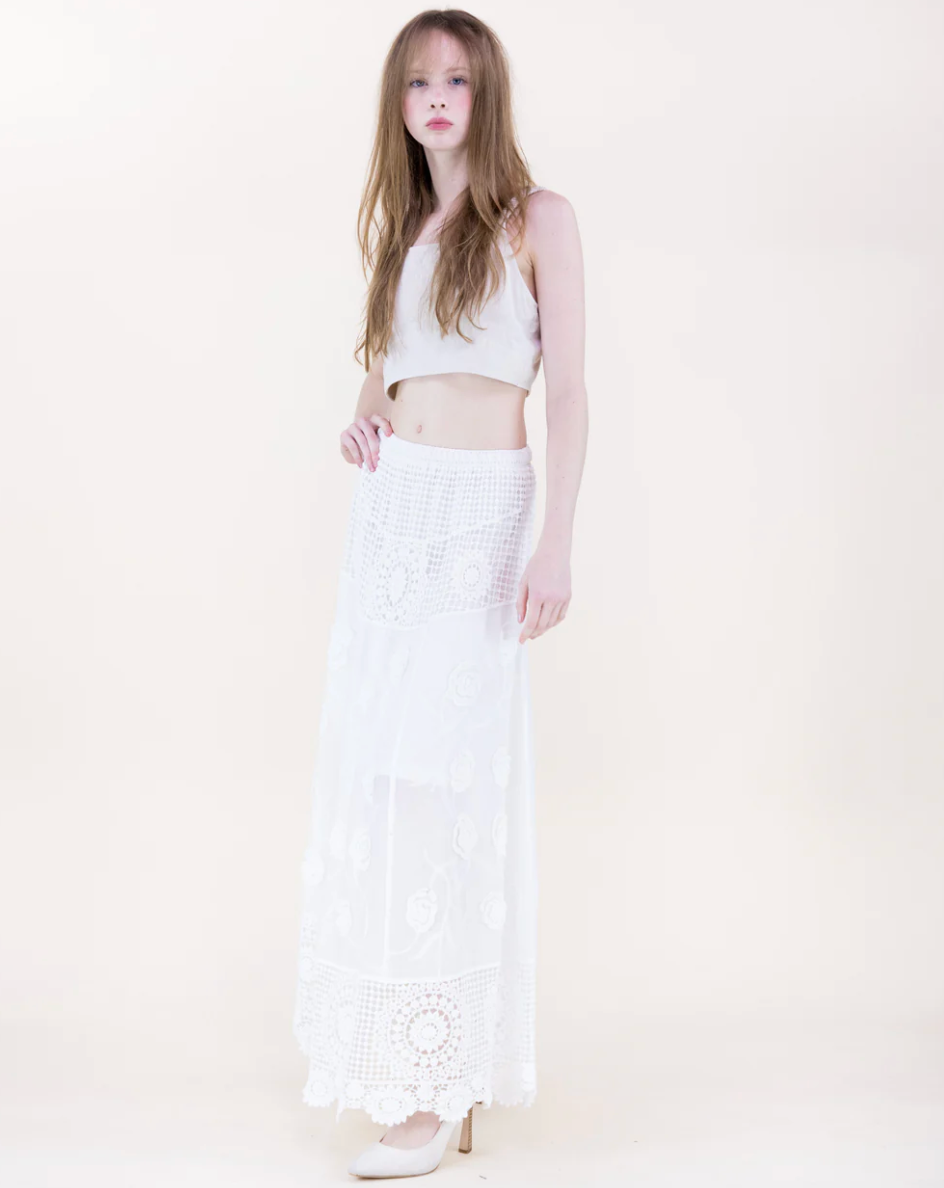 Woman wearing a white sleeveless top and white lace skirt on a light background