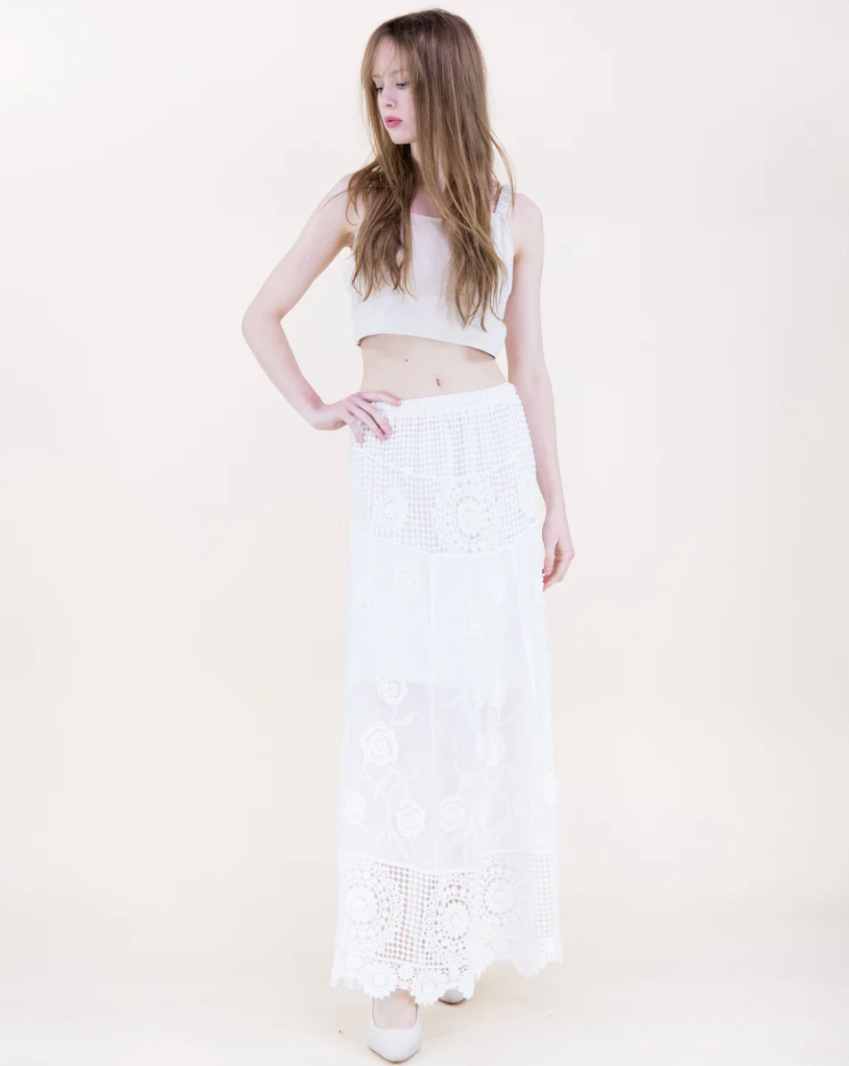 Woman wearing a white sleeveless top and white lace skirt on a plain background