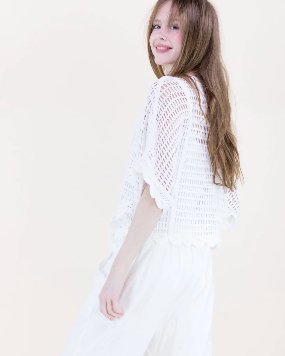 Young girl wearing a white crochet shrug against a plain background