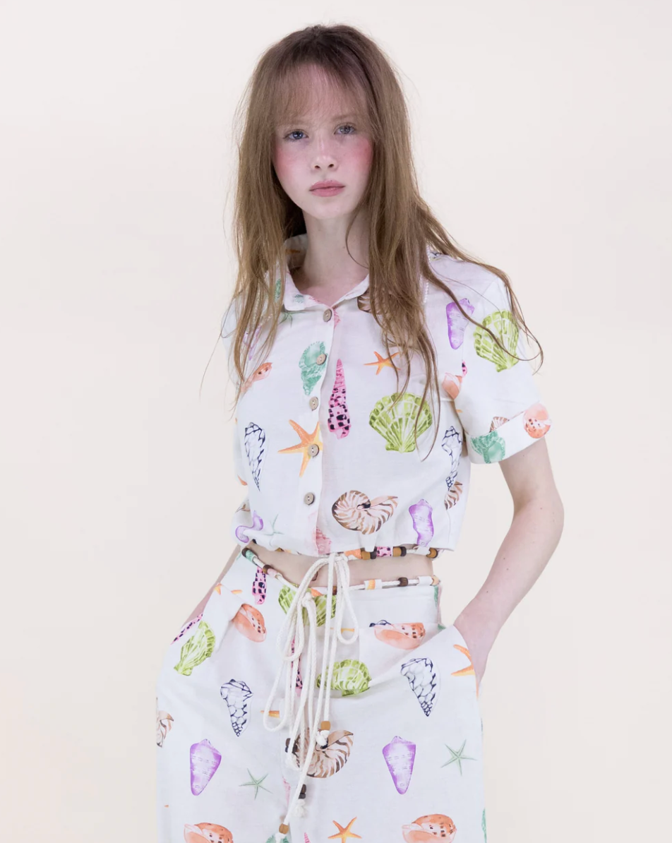 Person wearing a white shirt with colorful shell patterns on a plain background