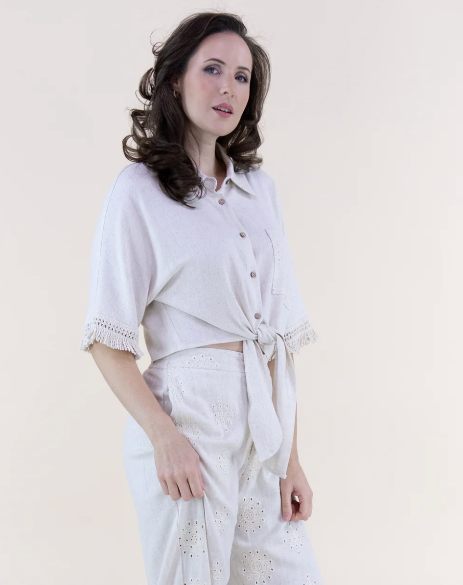 Woman wearing a light-colored outfit with a belt against a plain background