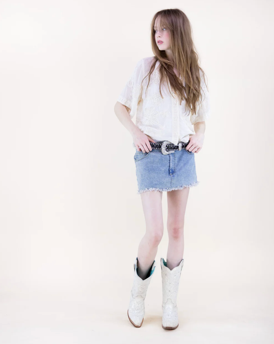 Woman wearing a white t-shirt, denim skirt, and white boots on a plain background
