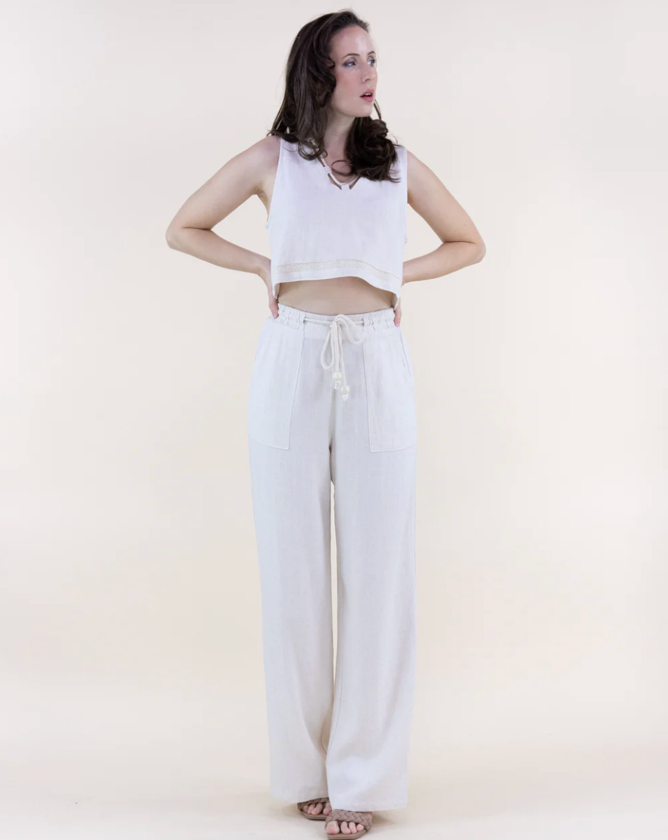 Woman wearing a white sleeveless top and wide-leg pants on a plain background