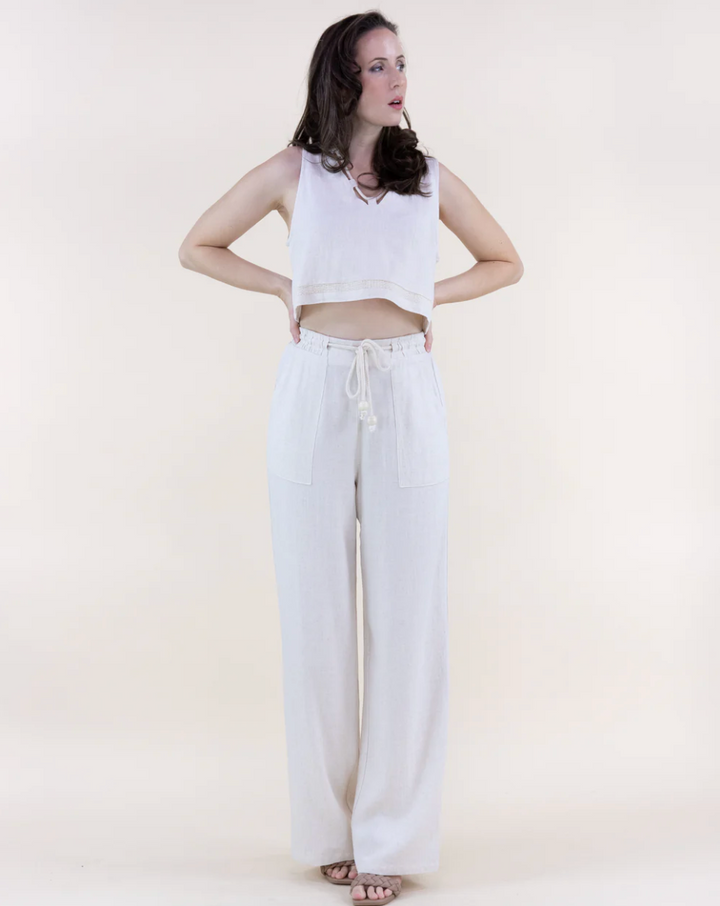 Woman wearing a white sleeveless top and wide-leg pants on a plain background