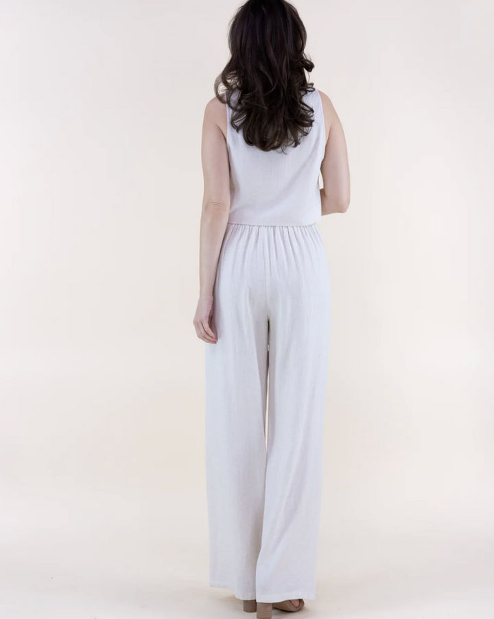 Woman wearing a white sleeveless jumpsuit on a plain background