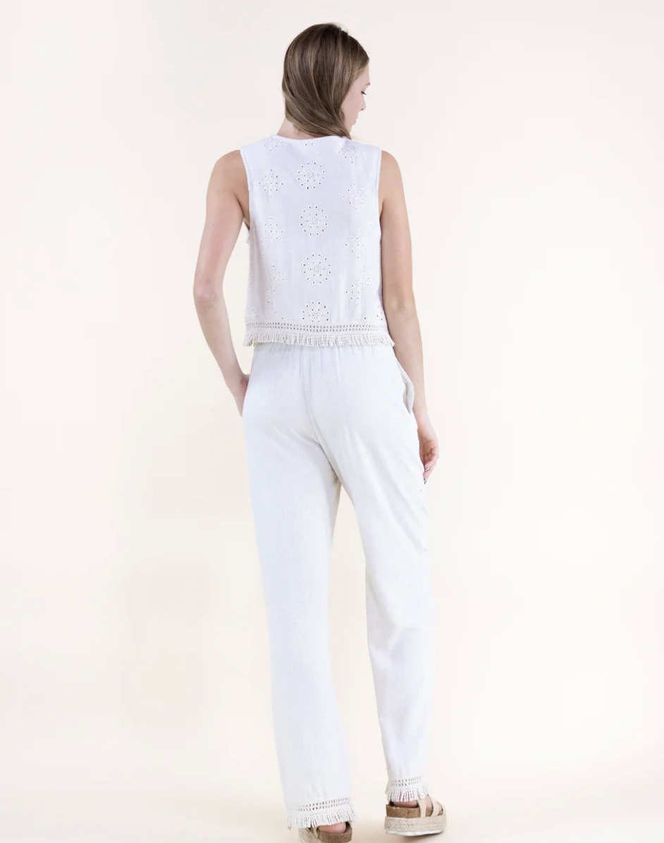 Woman wearing a white sleeveless top and pants on a light beige background