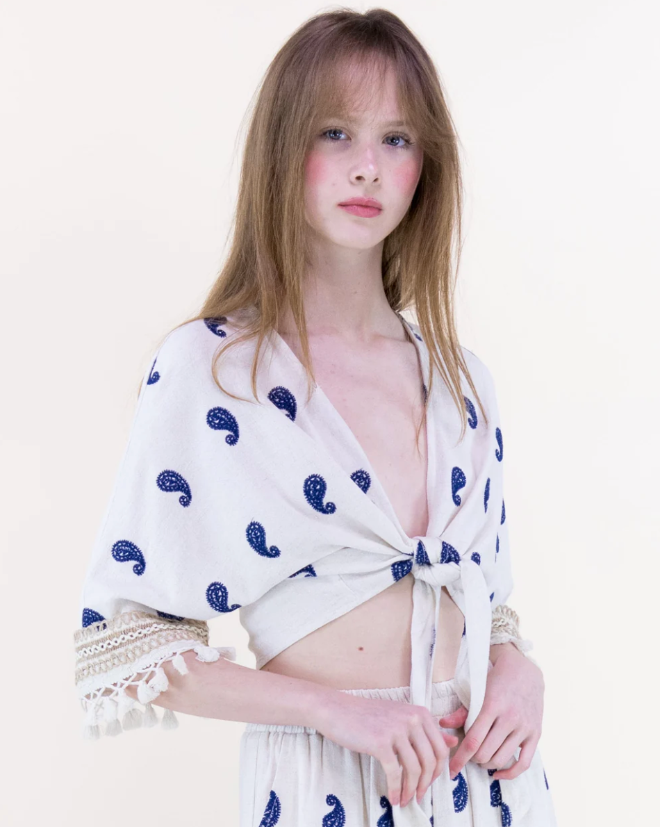 Woman wearing a white top with blue patterns on a plain background