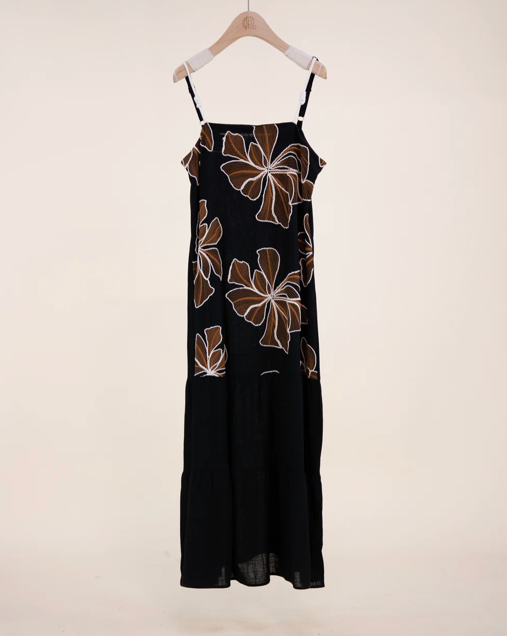Black dress with brown floral patterns on a hanger against a white background