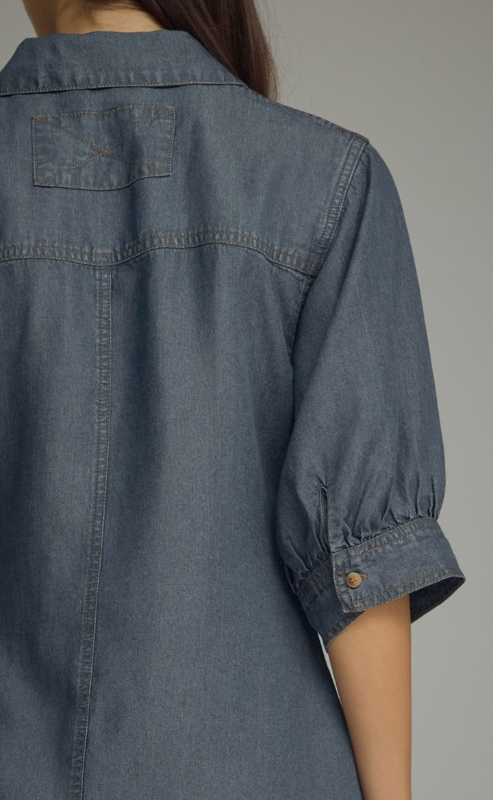 Close-up back view of a person wearing a blue-gray denim shirt dress with gathered elbow-length sleeves and a buttoned cuff.