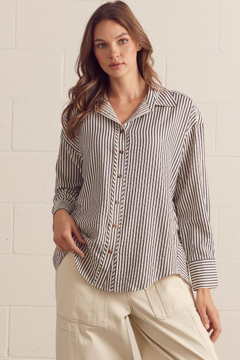 Woman wearing a striped shirt and beige pants against a white brick wall.