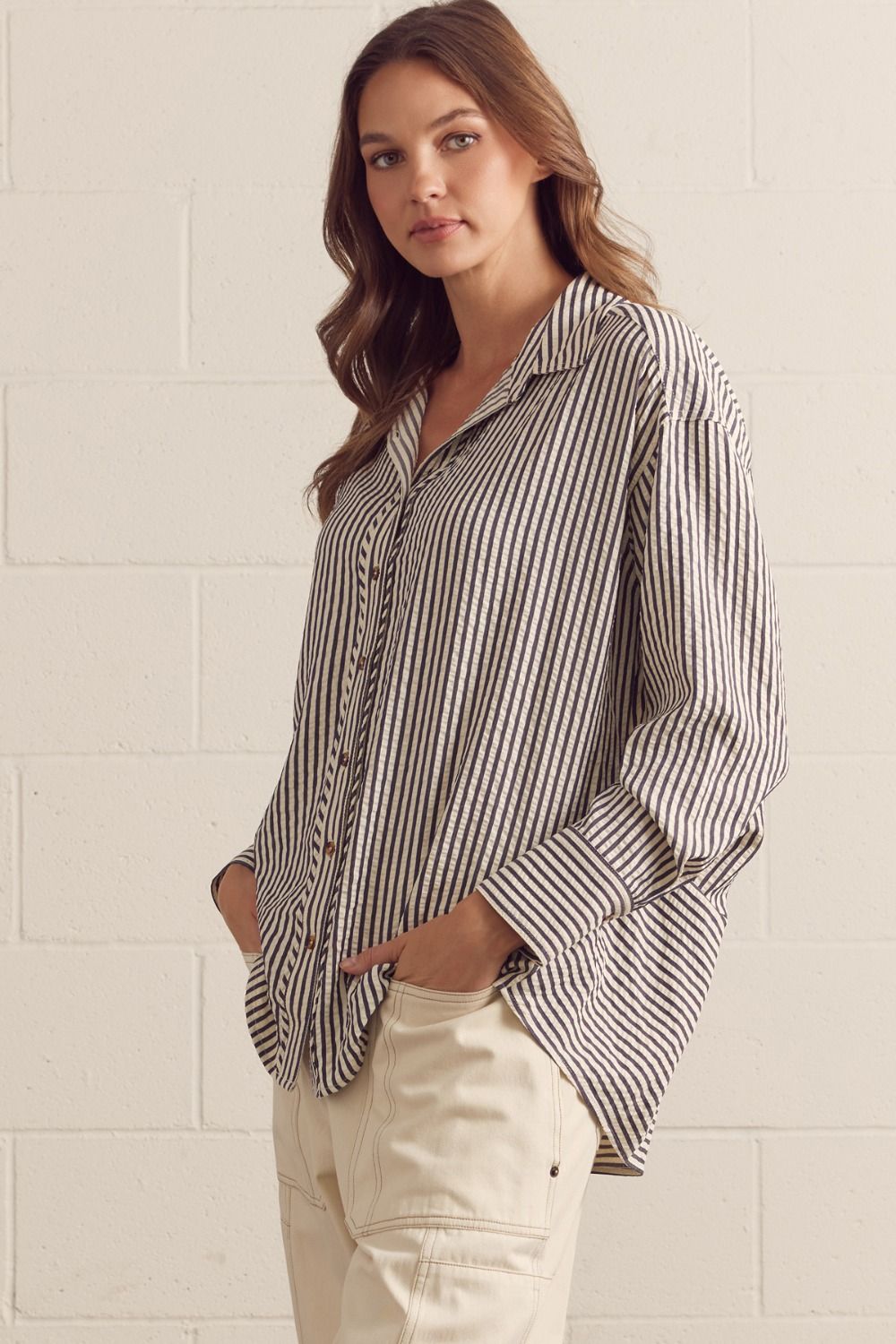 Woman wearing a striped shirt and beige pants against a light tiled wall.