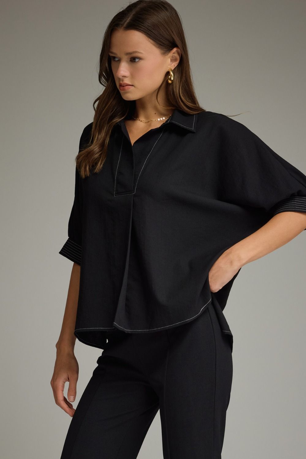 Woman wearing a black blouse and pants against a gray background