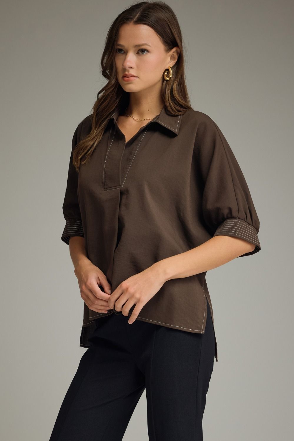 Woman wearing a brown blouse and black pants against a neutral background