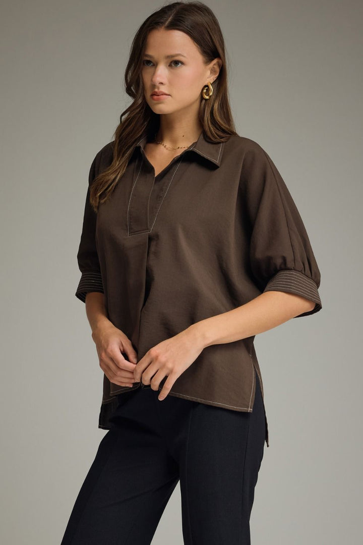Woman wearing a brown blouse and black pants against a neutral background