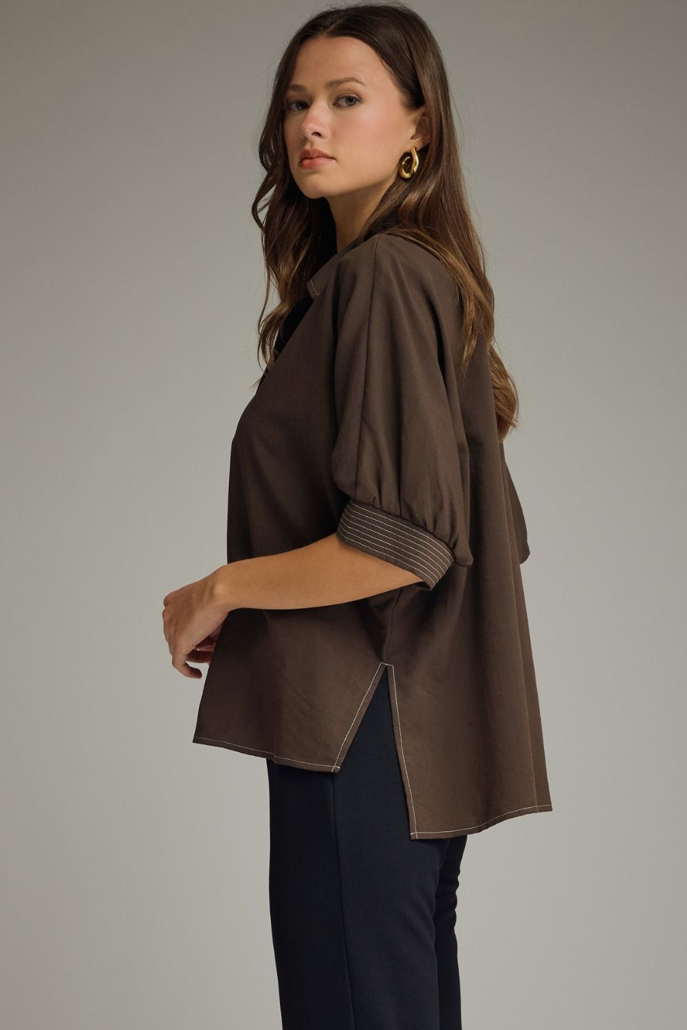 Woman wearing a brown jacket and black pants on a plain background
