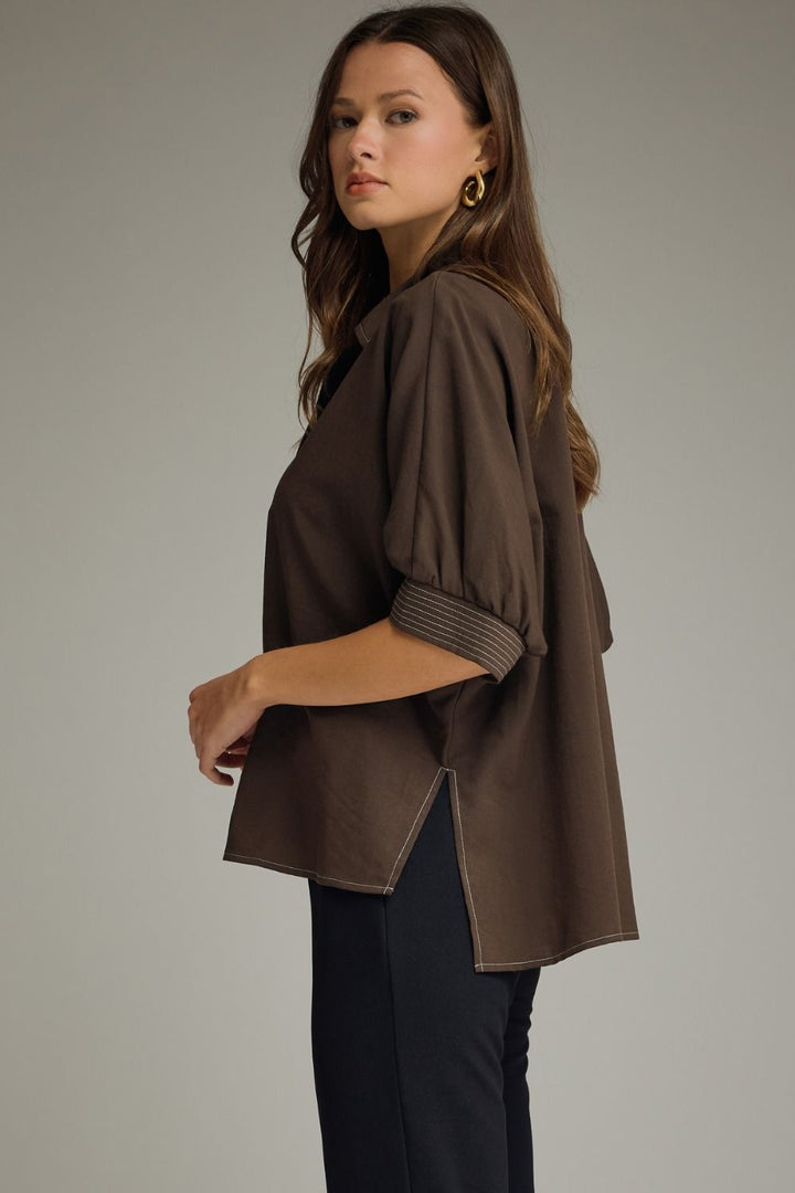 Woman wearing a brown jacket and black pants on a plain background