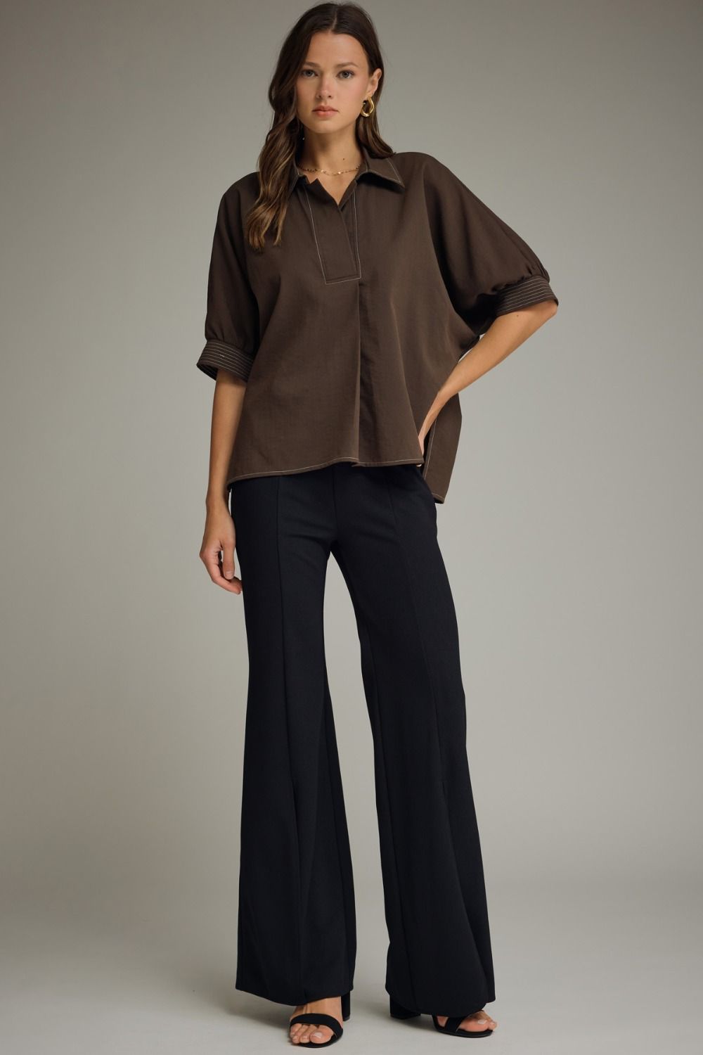 Woman wearing a brown blouse and black pants against a gray background