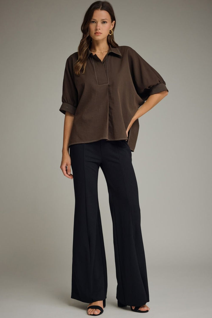 Woman wearing a brown blouse and black pants against a gray background