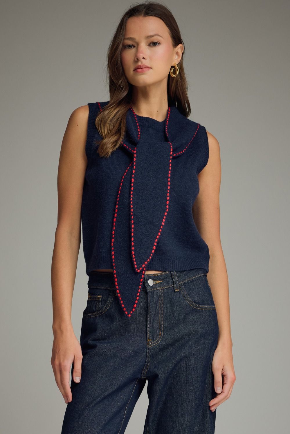 Woman wearing a navy sleeveless top with a red beaded necklace against a gray background