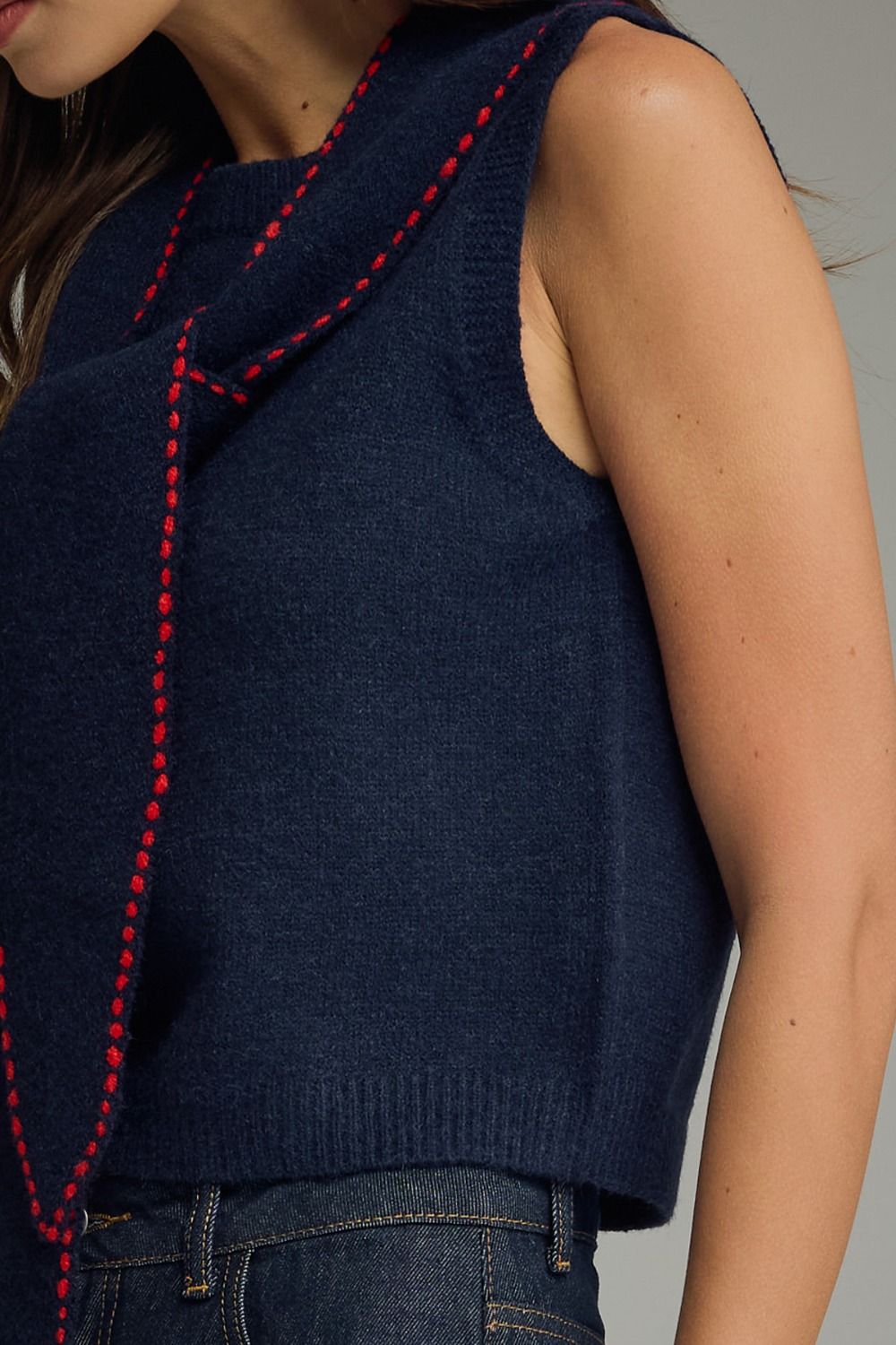 Navy blue sleeveless sweater with red stitching on a neutral background