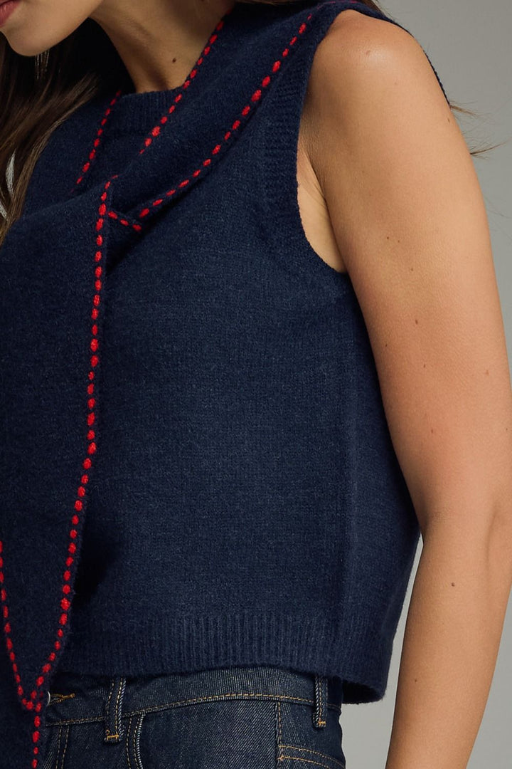 Navy blue sleeveless sweater with red stitching on a neutral background