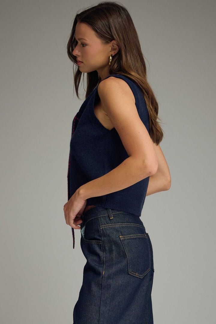 Woman wearing a navy sleeveless top and dark jeans against a plain background