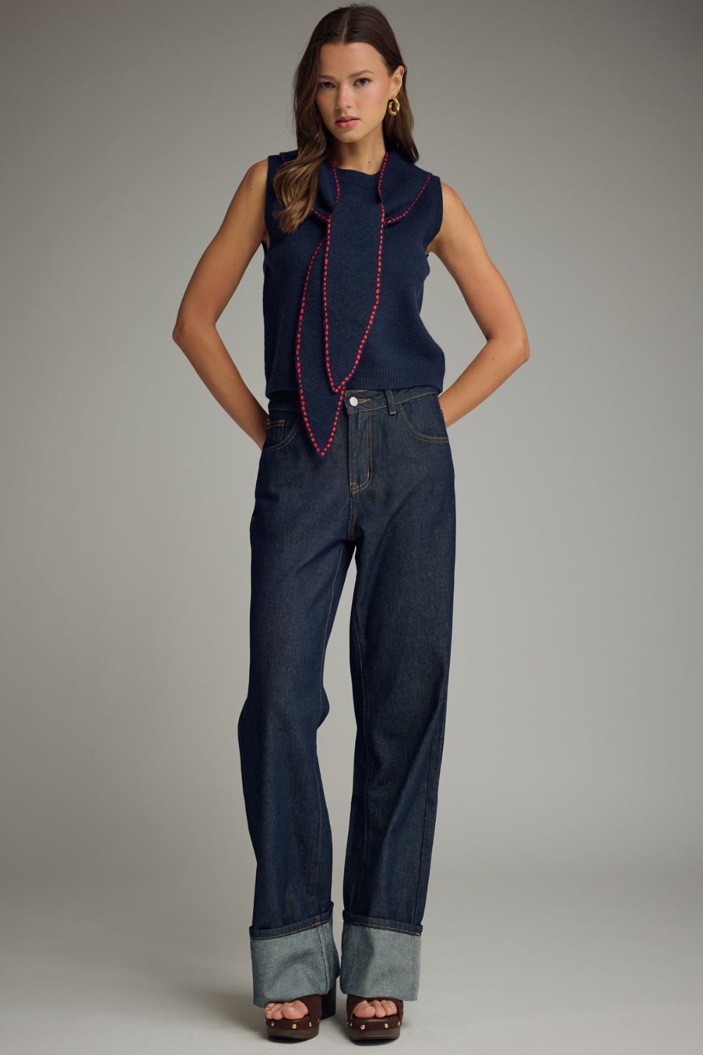 Woman wearing a sleeveless navy top with red trim and dark blue jeans on a gray background