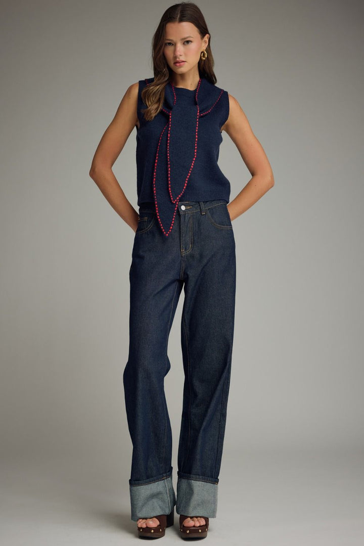 Woman wearing a sleeveless navy top with red trim and dark blue jeans on a gray background