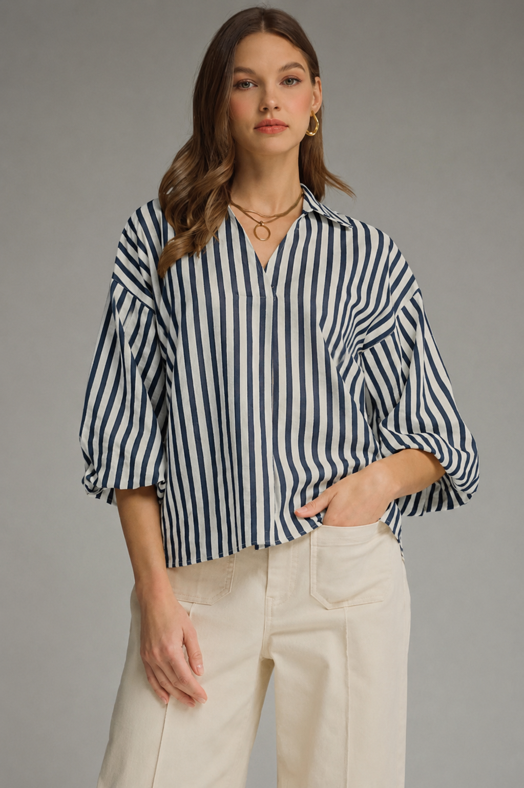 Woman wearing a navy and white striped shirt with beige pants on a gray background