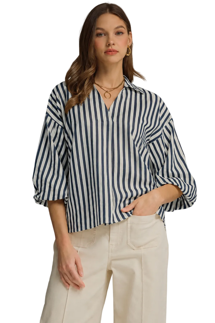 Woman wearing a navy and white striped shirt with beige pants on a gray background