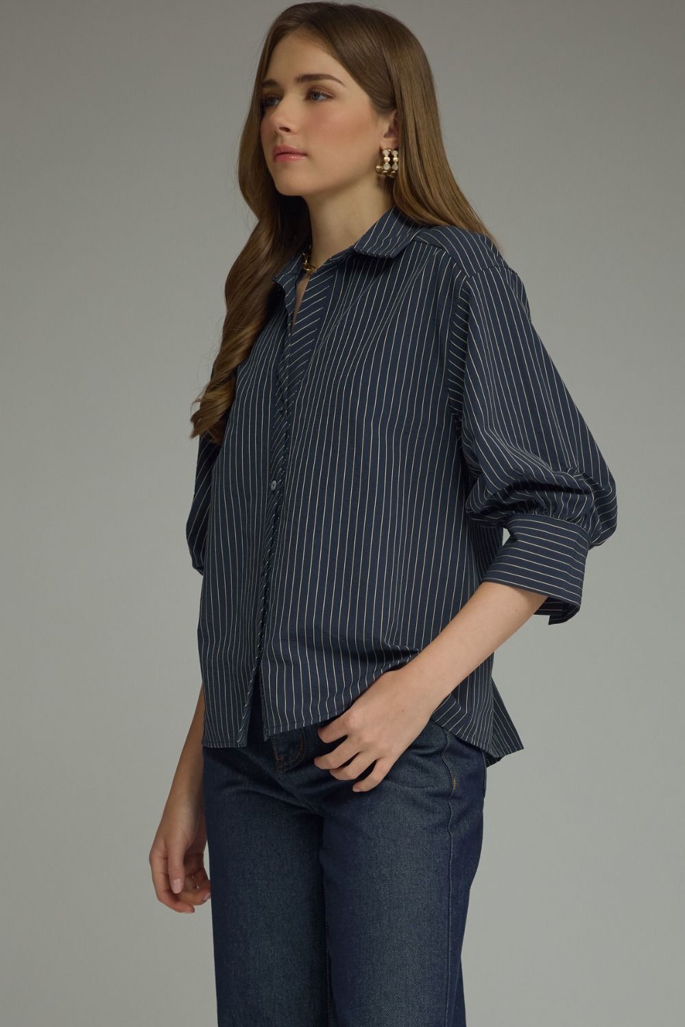 Woman wearing a dark blue striped shirt and jeans against a gray background