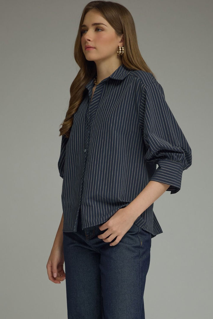 Woman wearing a dark blue striped shirt and jeans against a gray background
