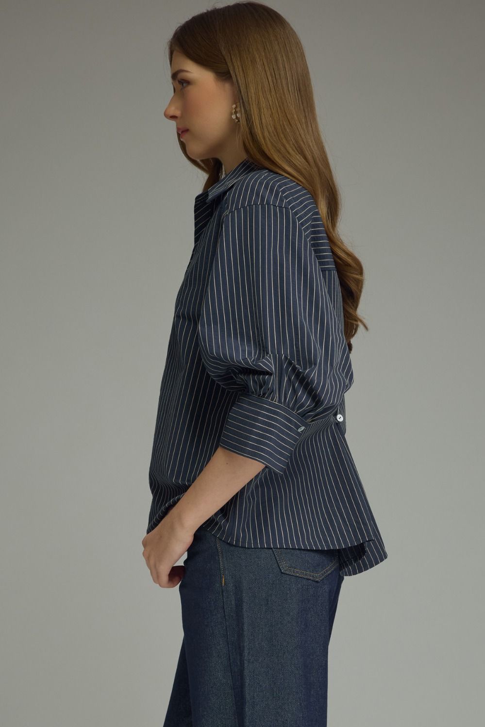 Woman wearing a dark blue pinstripe shirt and pants against a gray background