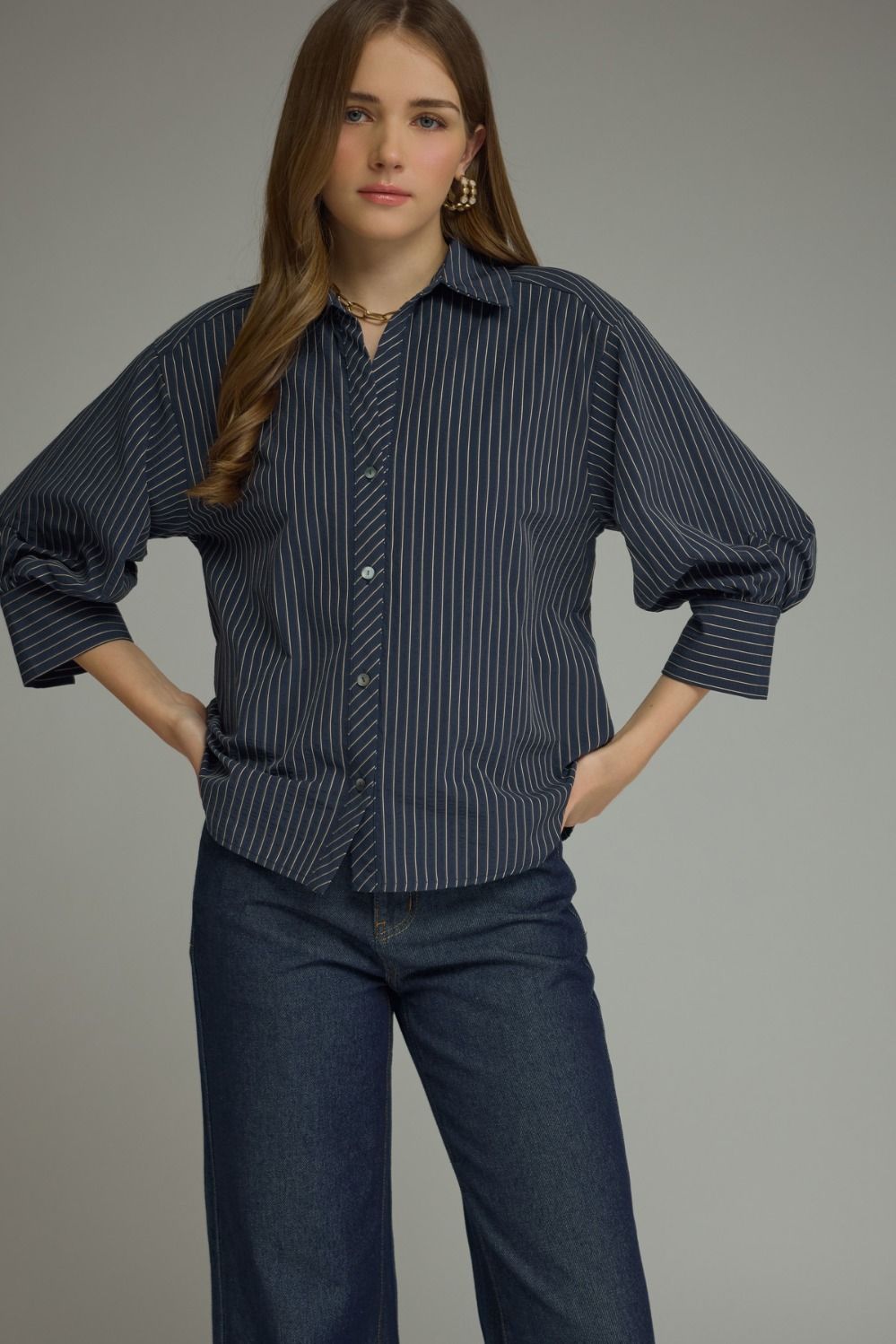 Woman wearing a dark blue pinstripe shirt and pants against a gray background