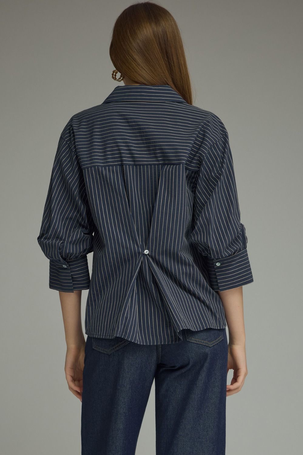 Person wearing a dark blue pinstripe shirt and jeans on a gray background