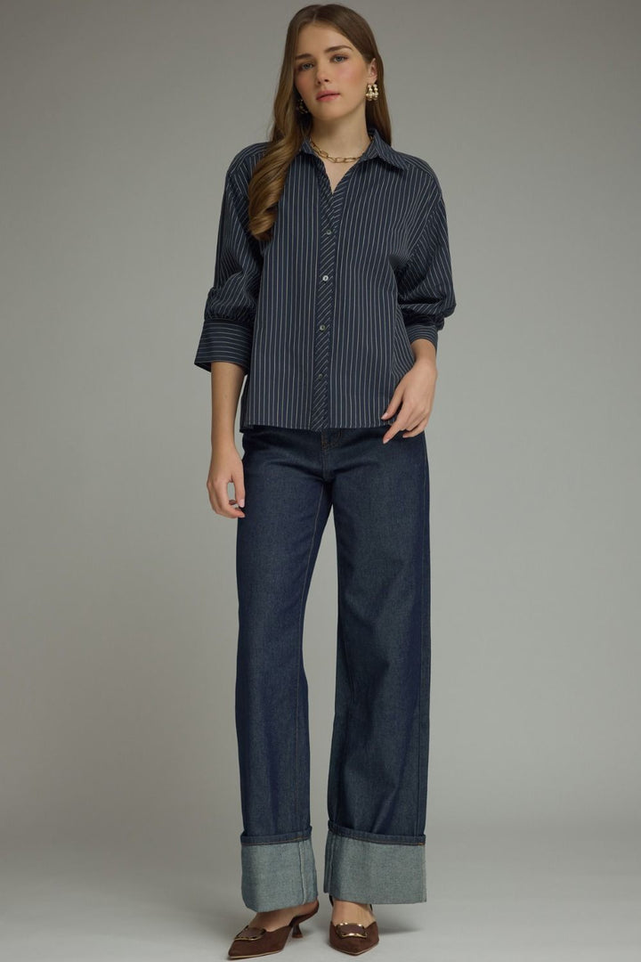 Woman wearing a dark blue striped shirt and jeans against a gray background