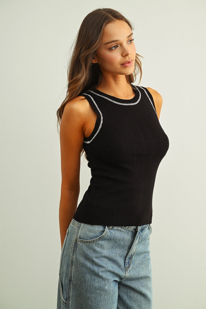 Woman wearing a black tank top with white trim and blue jeans on a light background