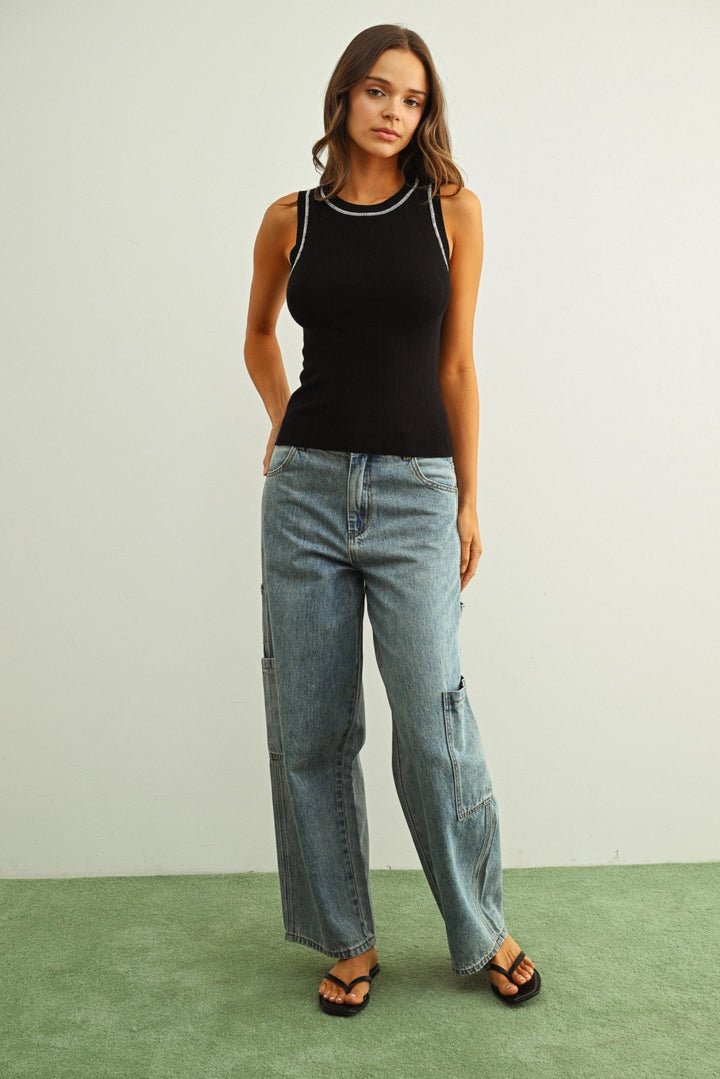 Woman wearing a black tank top and light blue jeans on a green floor with a white wall background