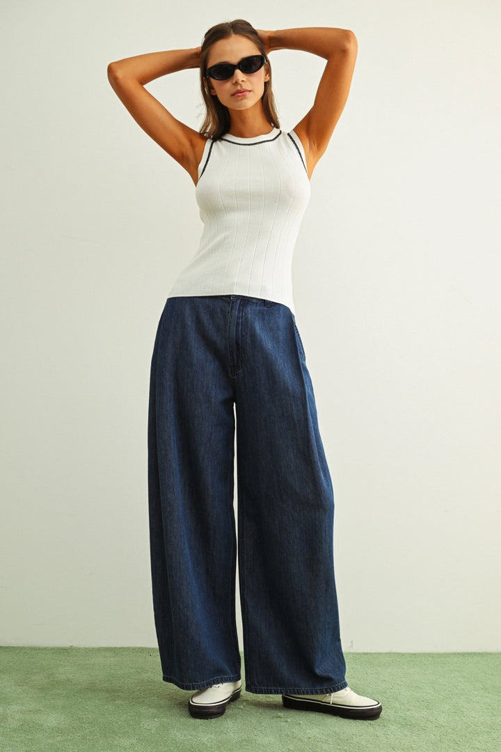 Woman wearing a white sleeveless top and blue wide-leg pants against a plain background