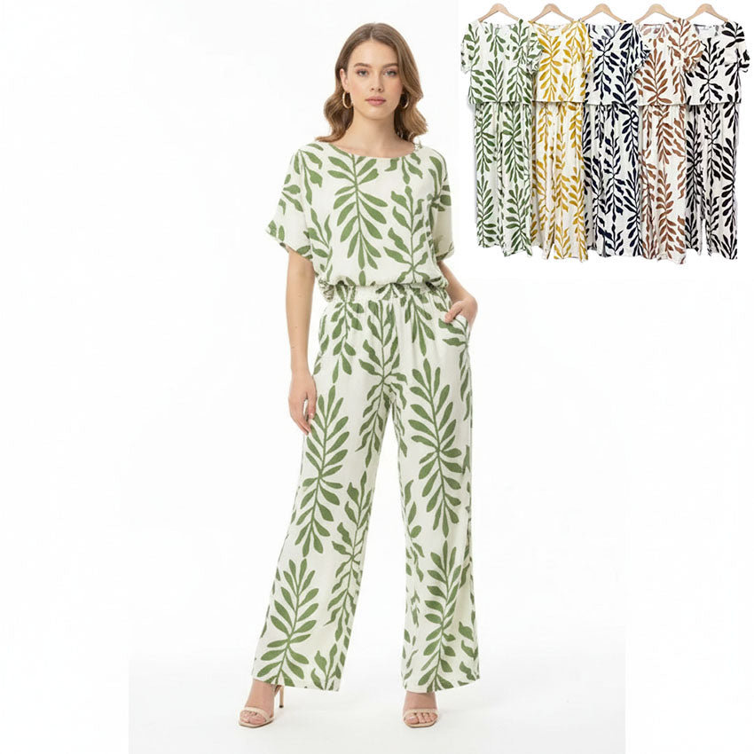 Woman wearing a leaf-patterned jumpsuit with additional jumpsuits displayed on hangers in the background.