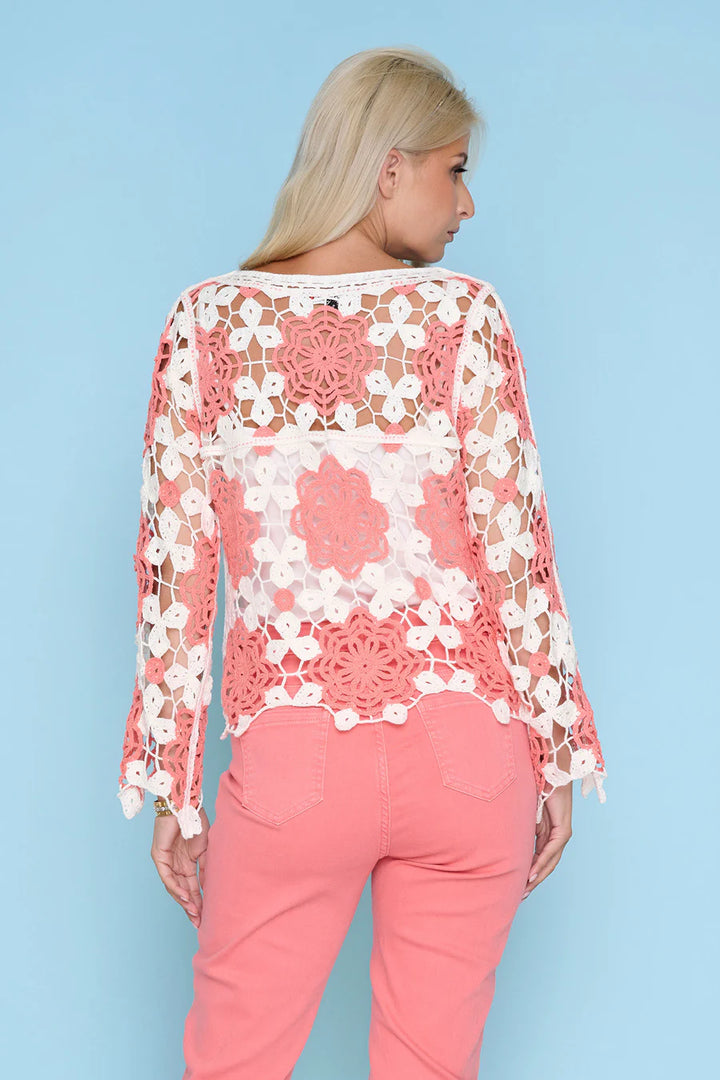 Woman wearing a coral and white lace top with pink pants against a light blue background