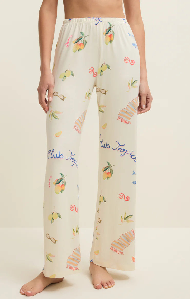 Person wearing pajama pants with tropical fruit and 'Club Tropicana' print on a plain background