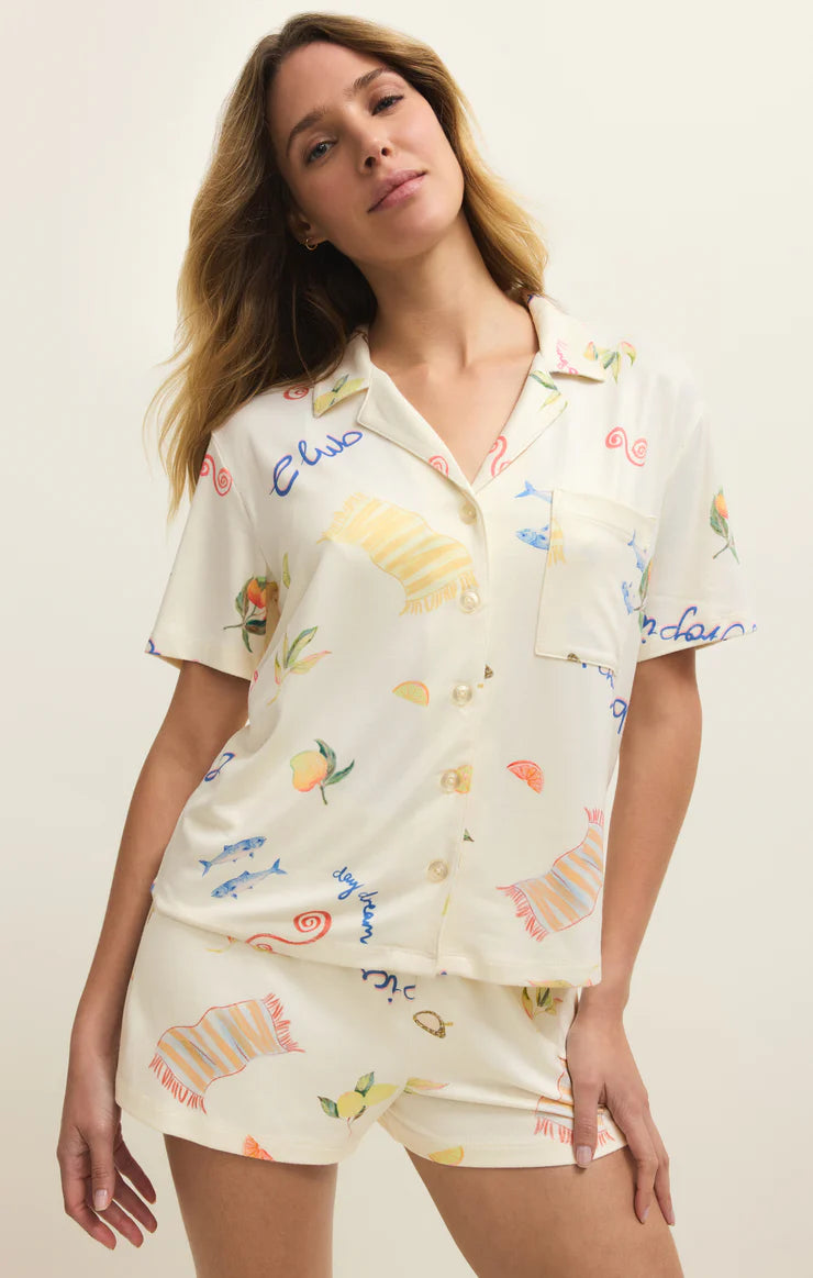 Woman wearing a cream-colored pajama set with colorful graphics and text on a plain background