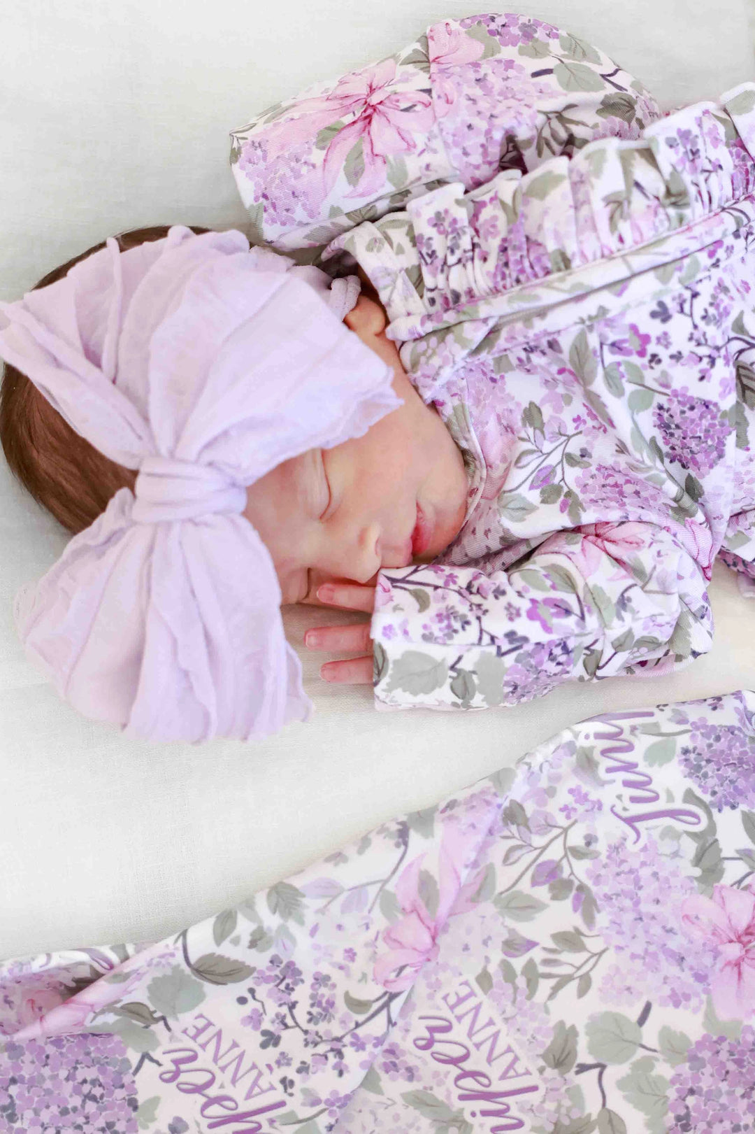 Newborn baby wrapped in a floral blanket with a matching headband on a white background